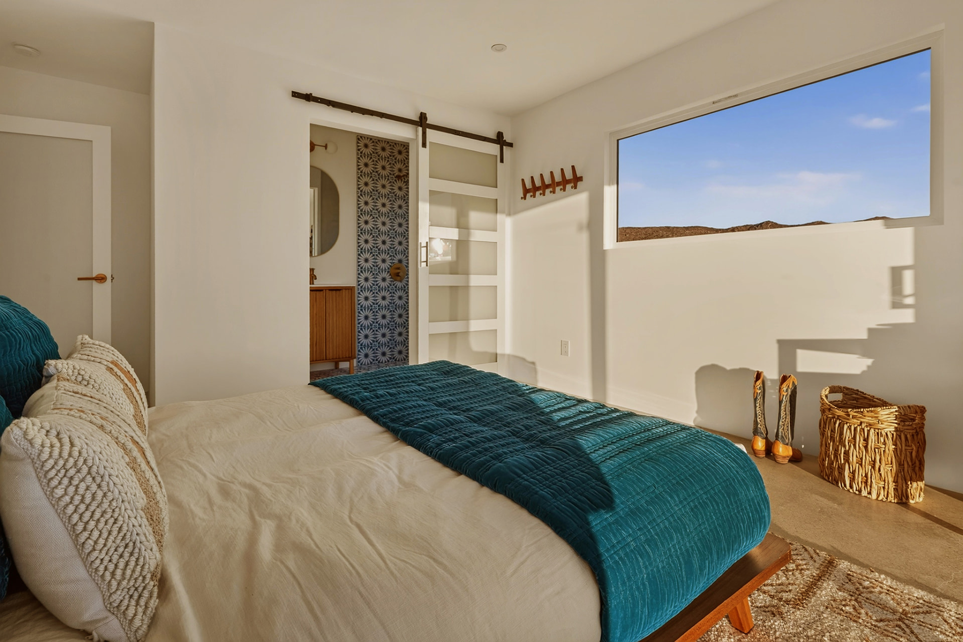 Bedroom with teal velvet quilt, barn door en suite and desert window